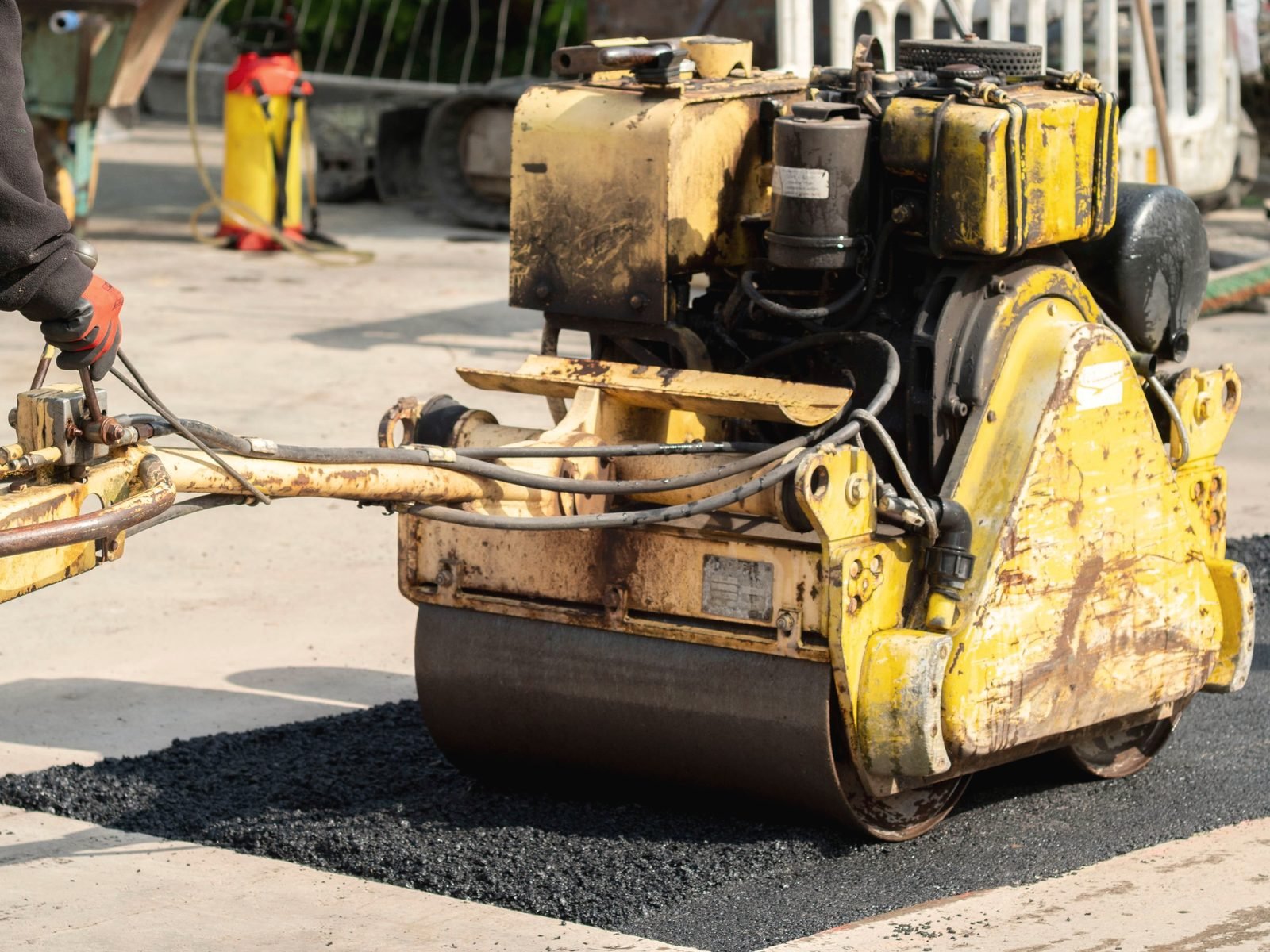 A walk-behind roller compacts a fresh asphalt patch.